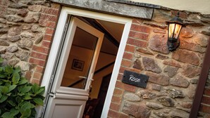 Une entrée en pierre, avec une porte, une plaque portant le nom « Rose » et une lanterne fixée au mur.