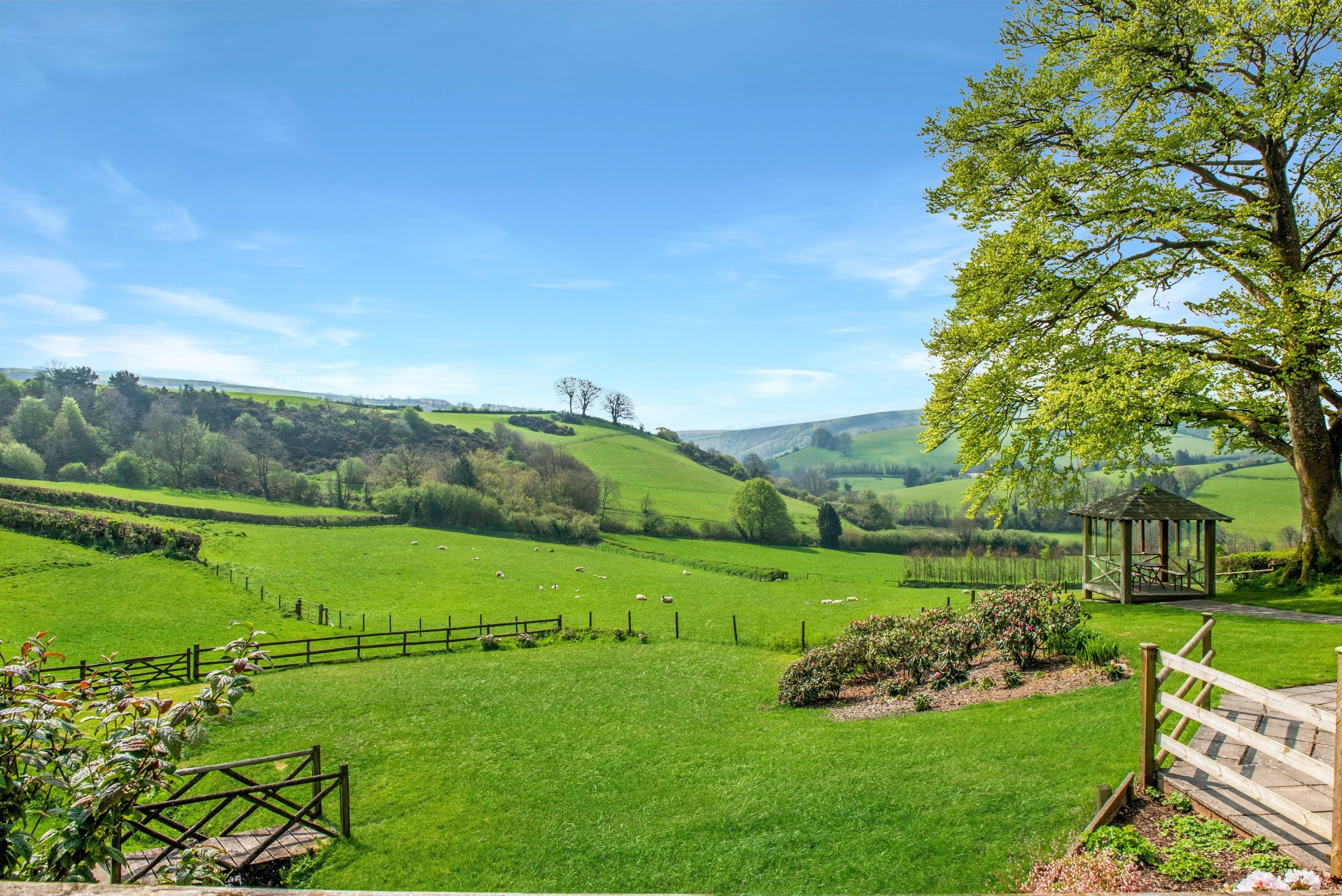 A lush green landscape with a gazebo, a fenced area, and a tree.