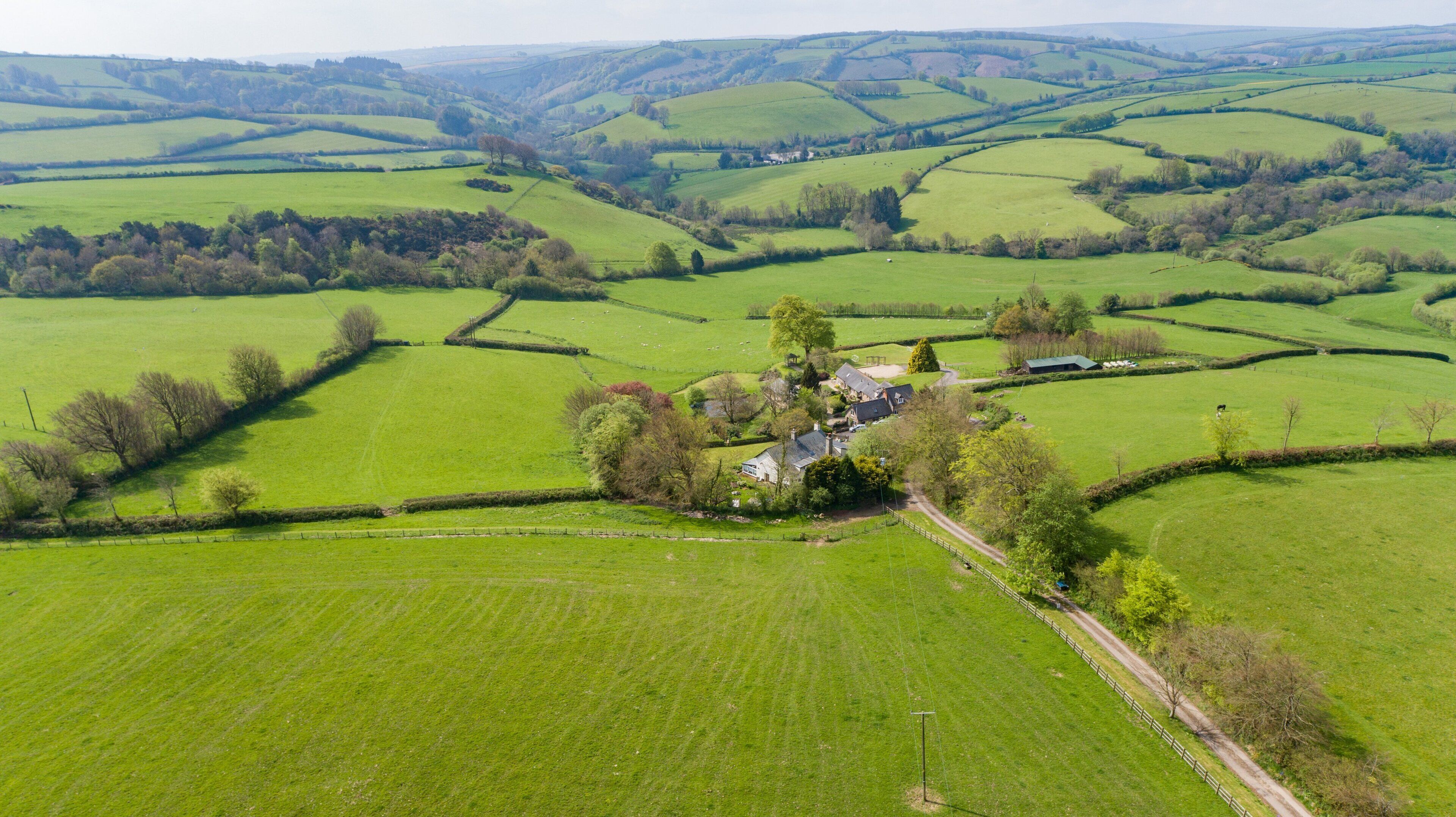 A rural landscape with rolling green fields, a small cluster of buildings, and a winding road.