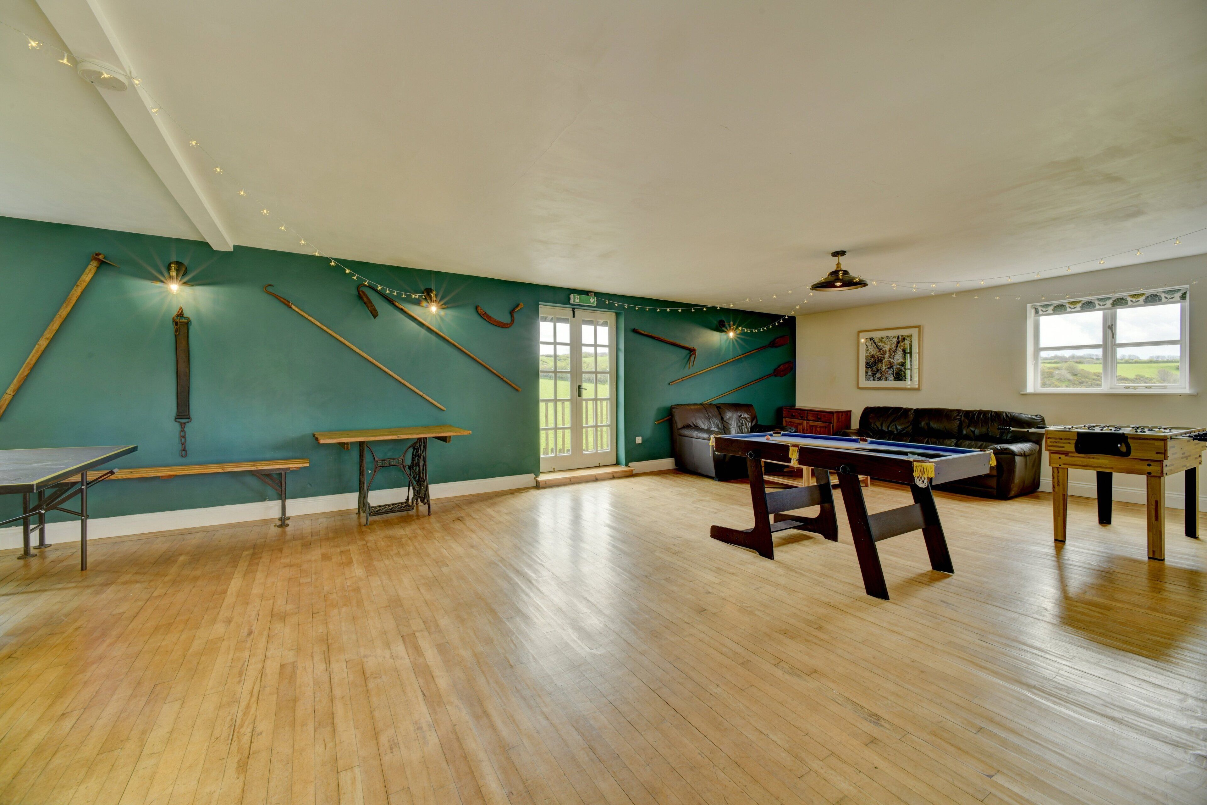 A spacious room with wooden flooring, a billiards table, a foosball table, and a pool table.