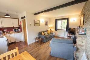 A living room with a sofa, a dining table, a kitchen area, and a stone wall.