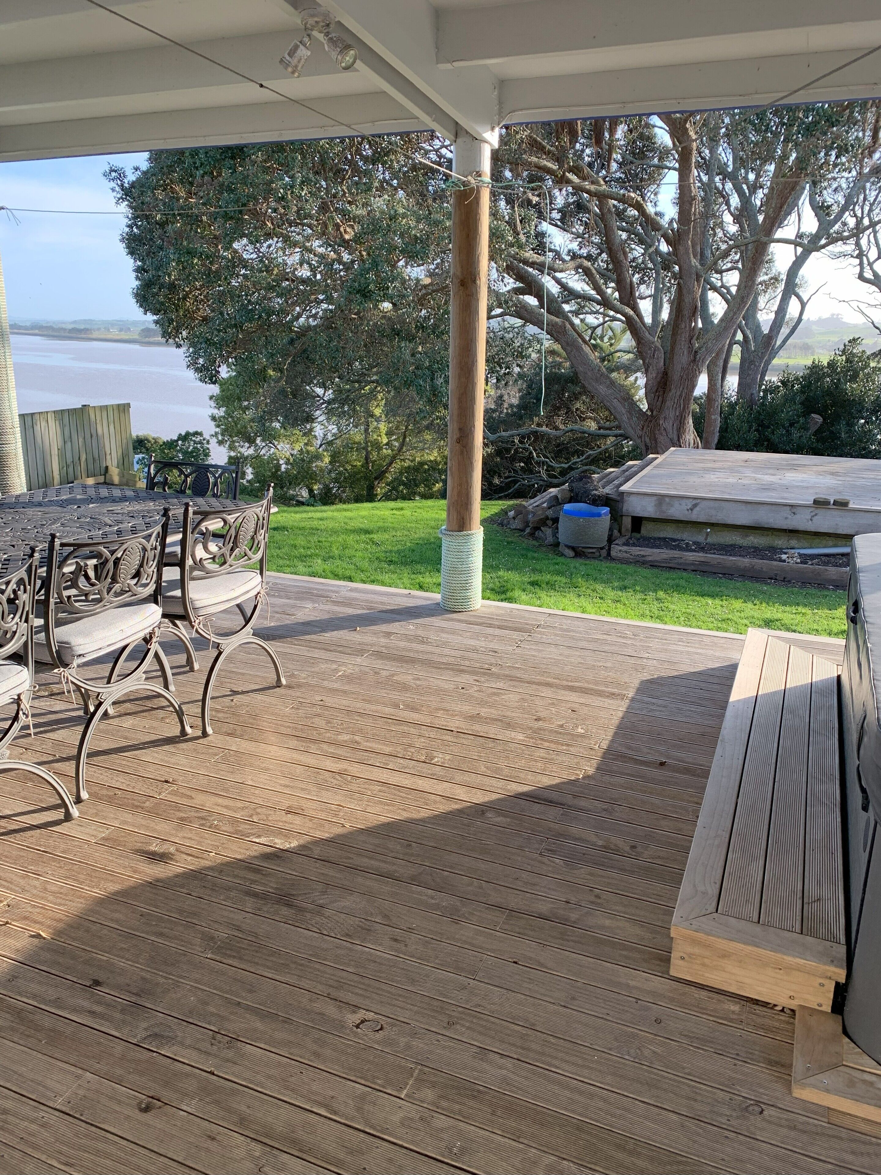 A covered outdoor patio with a wooden deck, metal chairs, and a table.