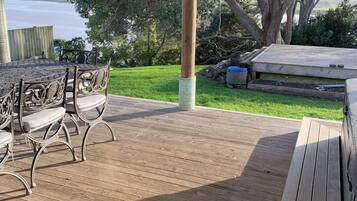 A covered outdoor patio with a wooden deck, metal chairs, and a table.