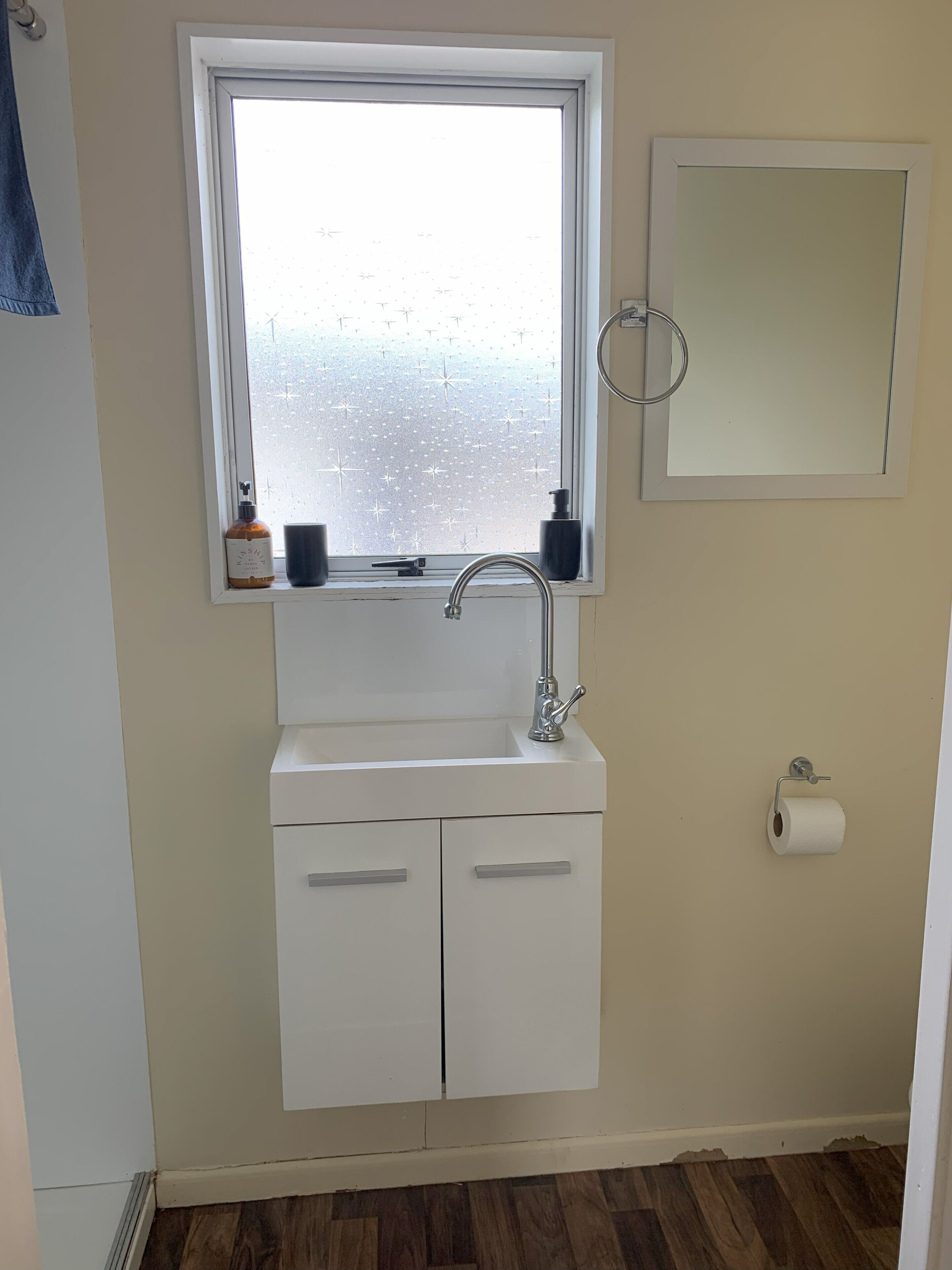 A bathroom with a window, a sink, a mirror, and a toilet paper holder.