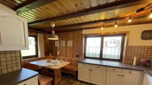 Uma cozinha acolhedora com armários de madeira, piso ladrilhado e uma área de jantar com mesa posta para dois.