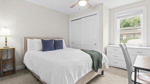 A bedroom with a bed, bedside table, lamp, dresser, chair, and window with a view.