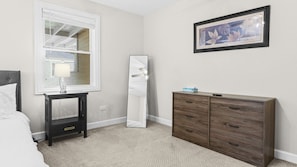 A bedroom with a bed, a nightstand, a dresser, a mirror, and a framed picture on the wall. - Ranch Home w/ Air Hockey & PacMan near Naval Base! (Libertyville)