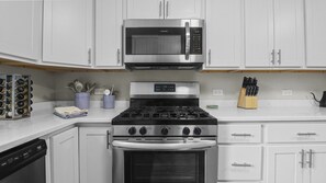 A kitchen with white cabinets, a stainless steel microwave, a gas stove, and an oven.
