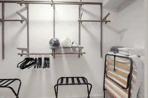 A compact room with a metal bed frame, a metal shelf with hanging items, and a metal rack with clothes. - Ranch Home w/ Air Hockey & PacMan near Naval Base! (Libertyville)