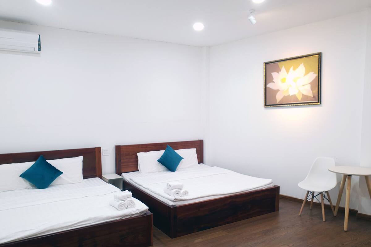 A hotel room with two wooden beds, white bedding, and a small white table.
