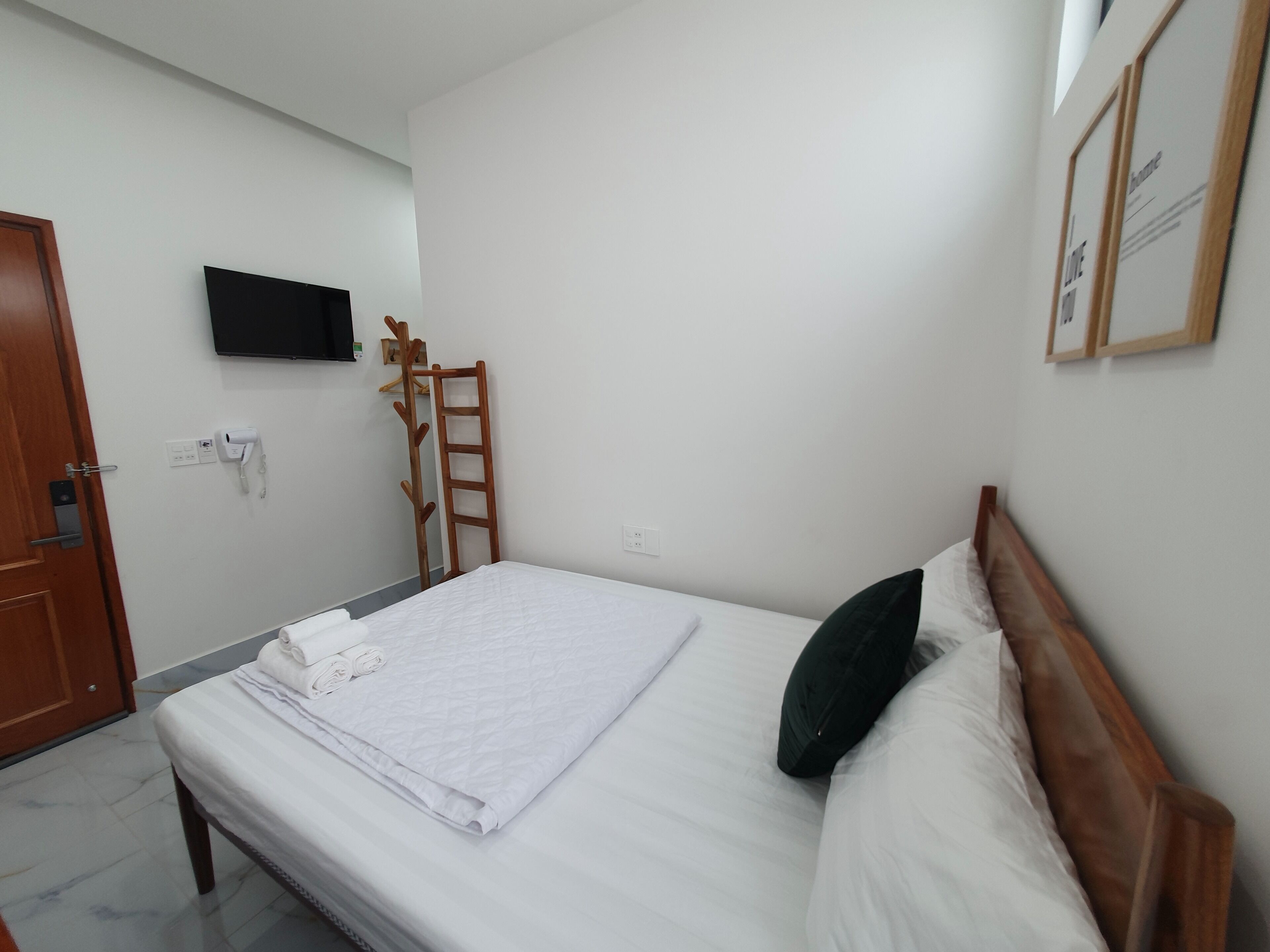 A neatly made bed with white linens, a wooden ladder leaning against the wall, a mounted television, and a door with a handle.