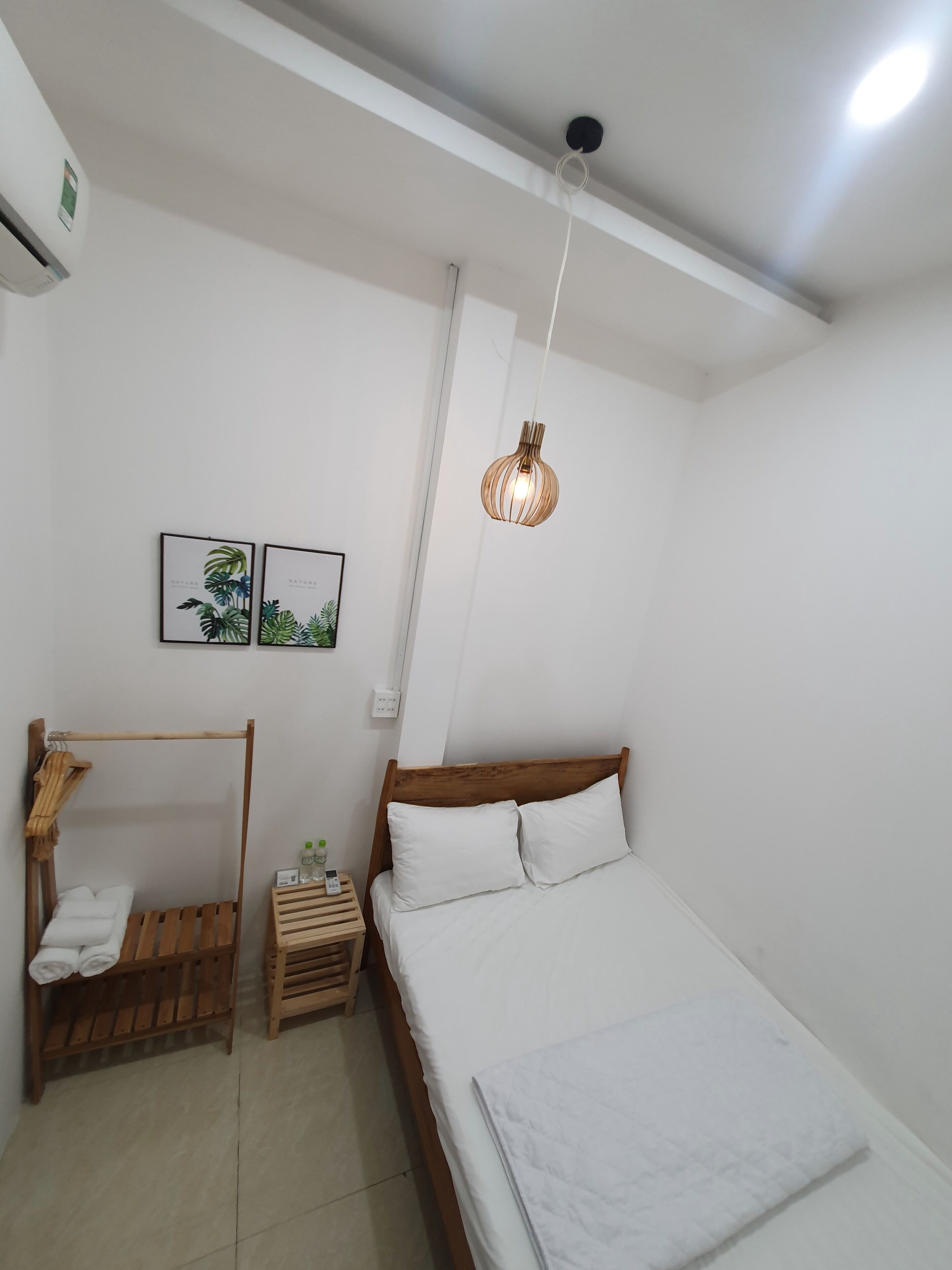 Quarto com cama de madeira, roupa de cama branca, luminária pendente e duas gravuras botânicas emolduradas na parede.