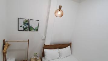 Quarto com cama de madeira, roupa de cama branca, luminária pendente e duas gravuras botânicas emolduradas na parede.