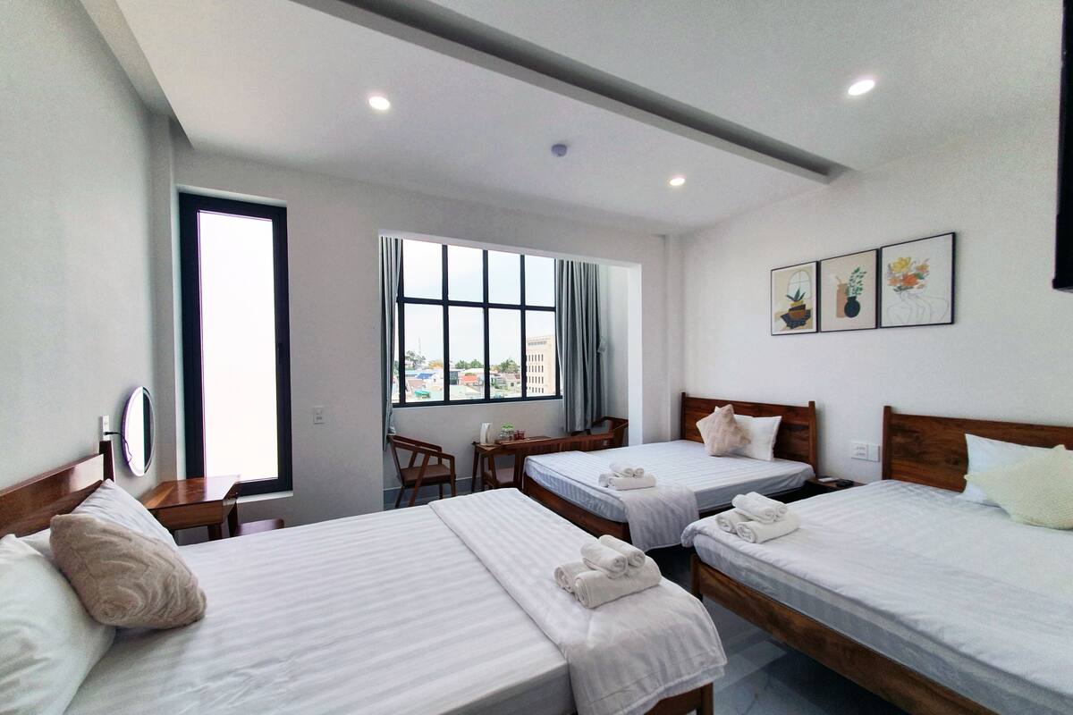 A hotel room with two beds, a desk, a chair, and a window with a view.