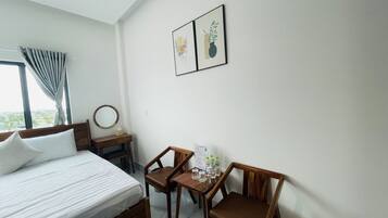 Habitación de hotel con una cama, dos sillas de madera, una mesita con botellas de agua y dos cuadros en la pared.