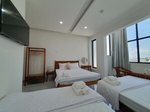 A hotel room with two beds, a wooden wardrobe, a bedside table, a mirror, and a window with a view. - HERO HOSTEL & BILLIARDS (Chau Doc)