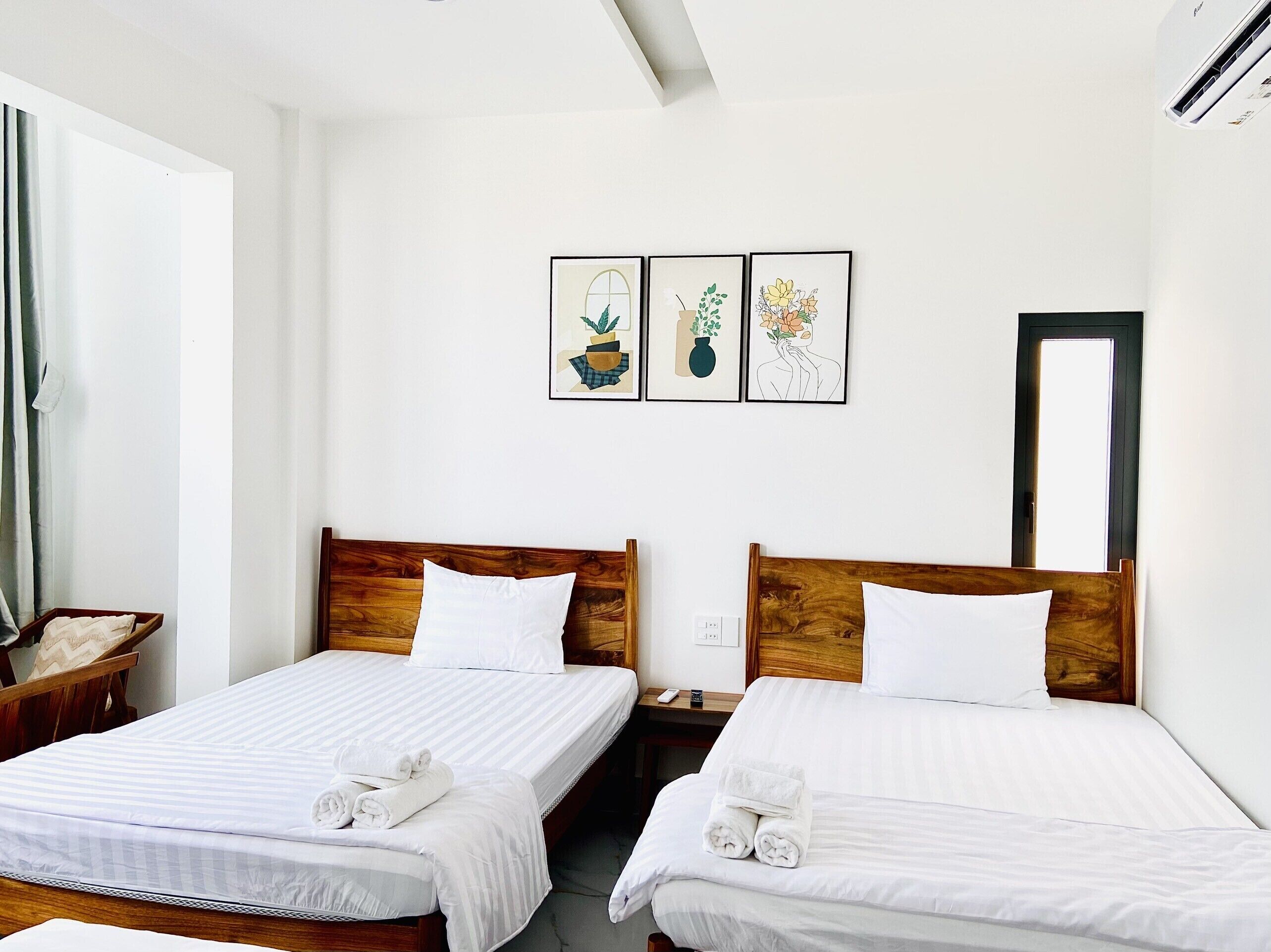 A hotel room with two beds, white linens, wooden headboards, and three framed artworks on the wall.