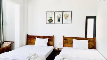A hotel room with two beds, white linens, wooden headboards, and three framed artworks on the wall.