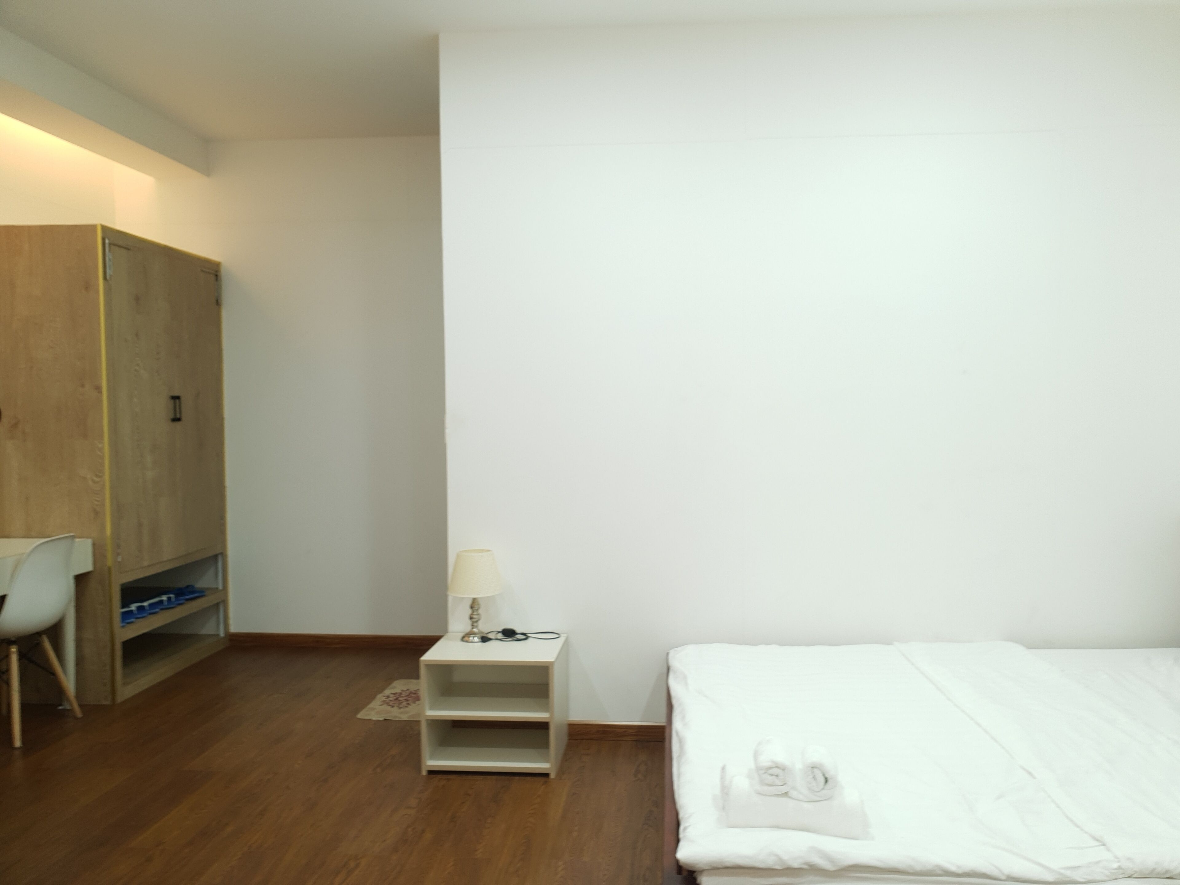Une chambre à coucher avec une armoire en bois, une table de chevet avec une lampe, une chaise et un lit soigneusement fait.