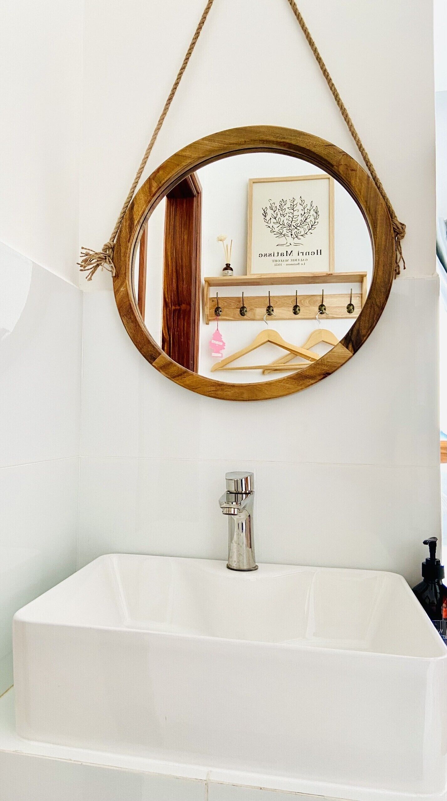 Une salle de bain avec une baignoire blanche, un miroir à cadre en bois et une étagère en bois munie de crochets et d’un tableau encadré.