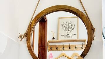 A bathroom with a white bathtub, a wooden-framed mirror, and a wooden shelf with hangers and a framed picture.