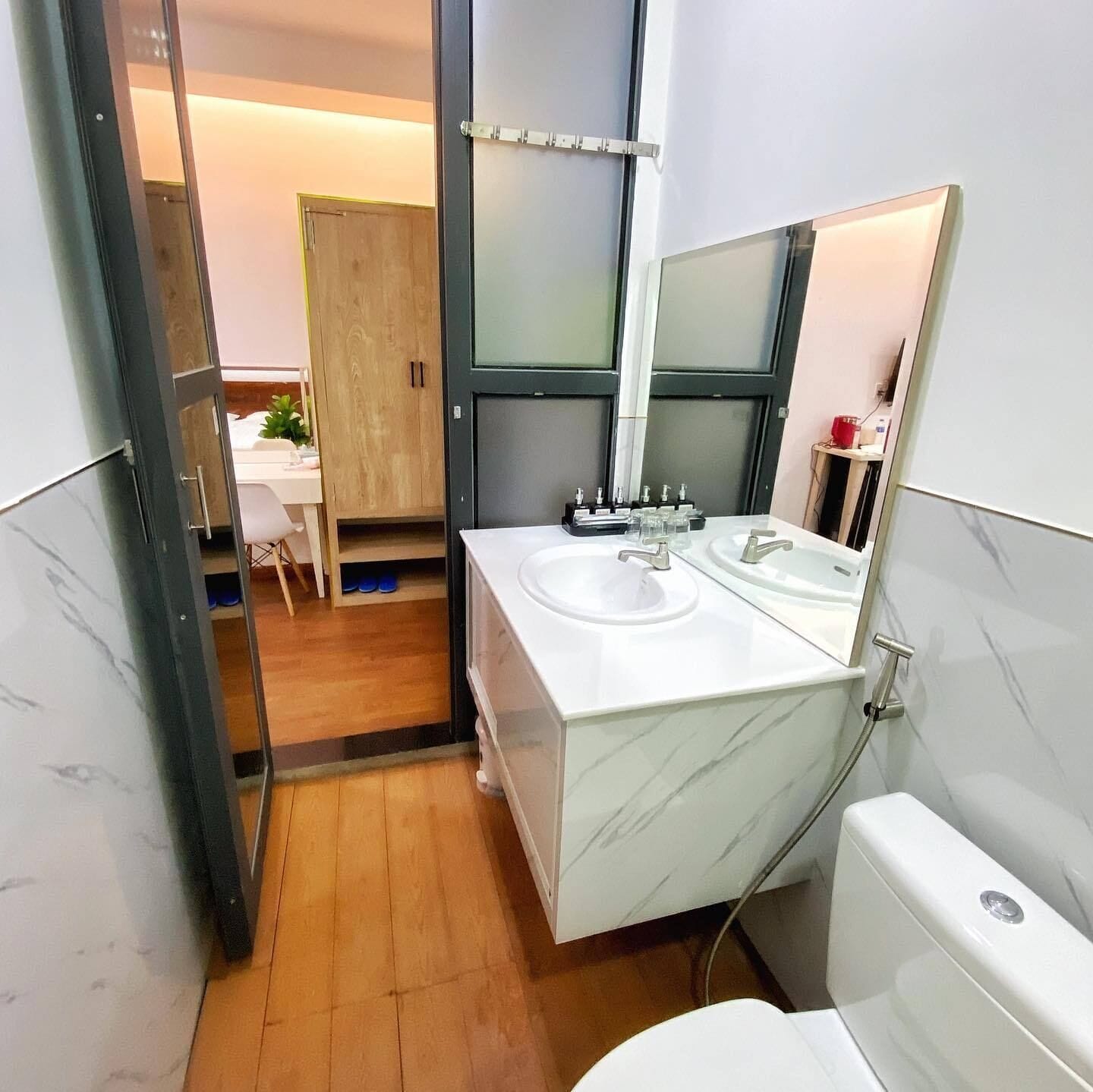 Un baño moderno con tocador de mármol, dos lavamanos, un espejo grande y un inodoro.