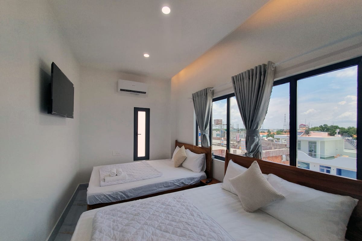 A hotel room with two beds, a TV mounted on the wall, and a window with curtains.