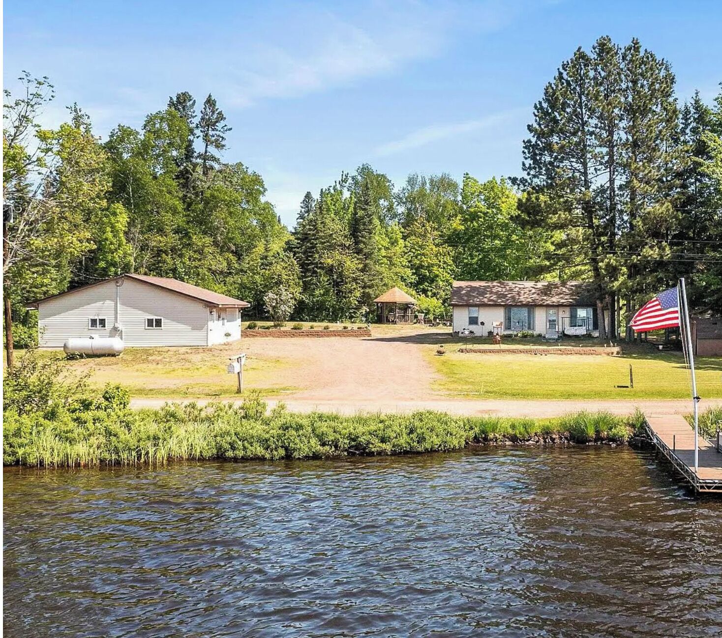 Une propriété située au bord de la rivière, comprenant une petite cabane, un bâtiment plus grand et un drapeau américain.