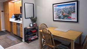 Hotelkamer met een houten eettafel, een stoel, een plank met gezelschapsspellen, een ingelijste kaart aan de muur, en een kitchenette met houten kastjes en een spoelbak.