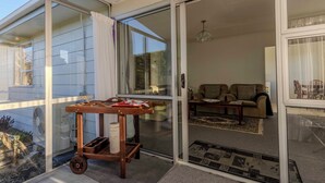 Una sala moderna con un conjunto de sofá, un carrito de madera con objetos y un ventanal corredizo que da a un balcón.