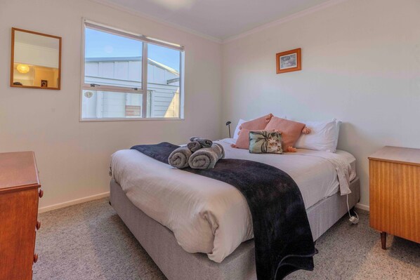 A bedroom with a bed, a window, a dresser, and a bedside table.