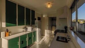 Cocina pequeña con gabinetes verdes, microondas, refrigerador y lavamanos.