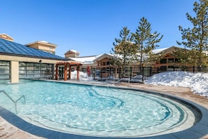 Una piscina con un jacuzzi, rodeada de edificios de diseño moderno, y un terreno cubierto de nieve.