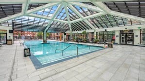 Ein Hallenbad mit Glasdach, umgeben von Liegestühlen und einer Poollandschaft.
