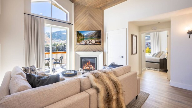 Ein großzügiges Wohnzimmer mit Kamin, einer Couch und Blick auf Berge durch große Fenster.