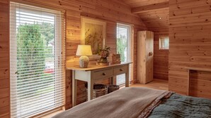 Un dormitorio de cabaña de madera con una cama, cómoda y una ventana pequeña con persianas.