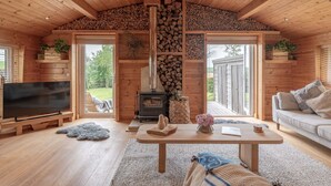 Un interior de cabaña acogedor con techo de madera, chimenea, televisor y sofá.