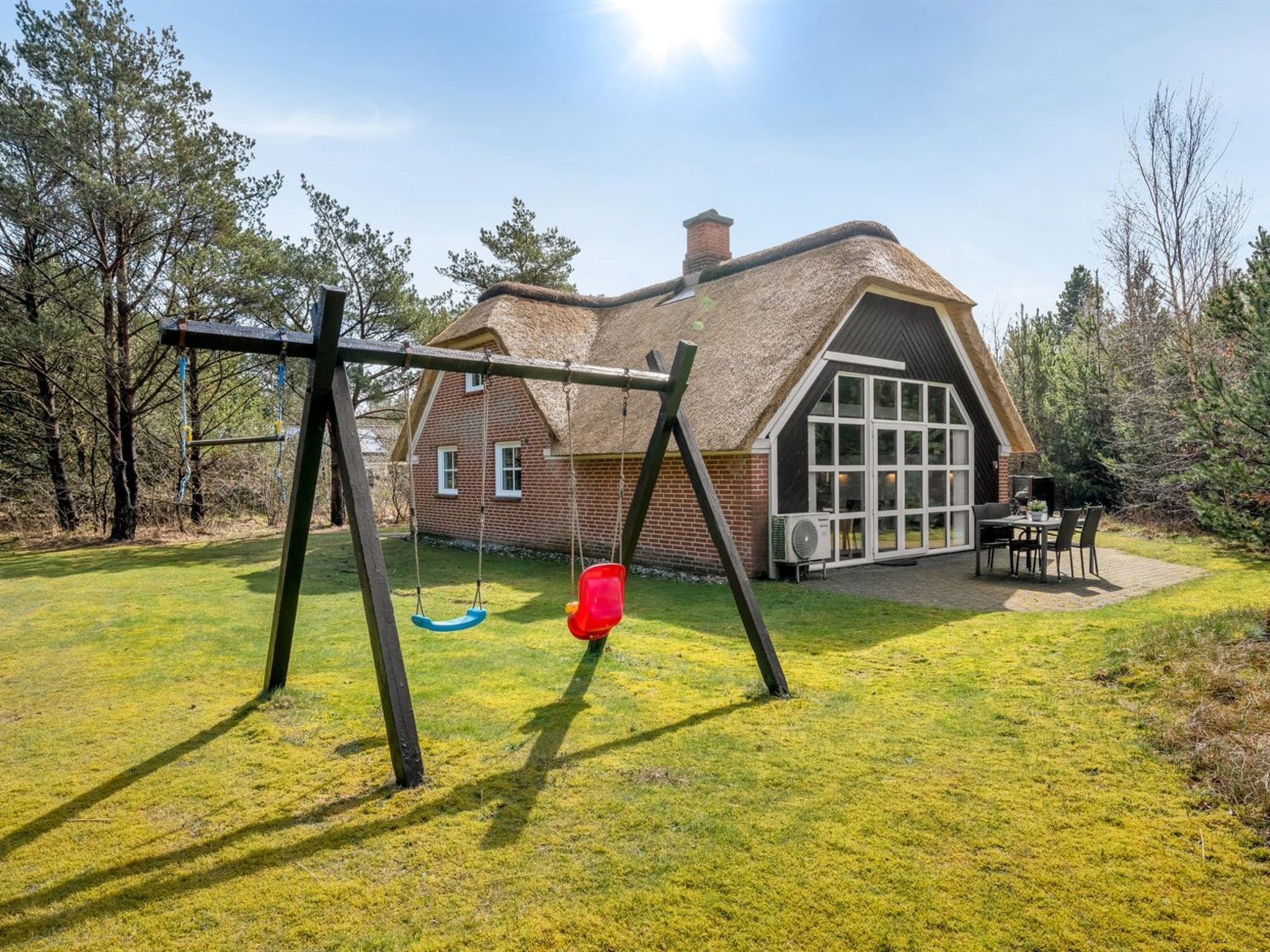 A house with a thatched roof, a swing set, and a patio with outdoor furniture.