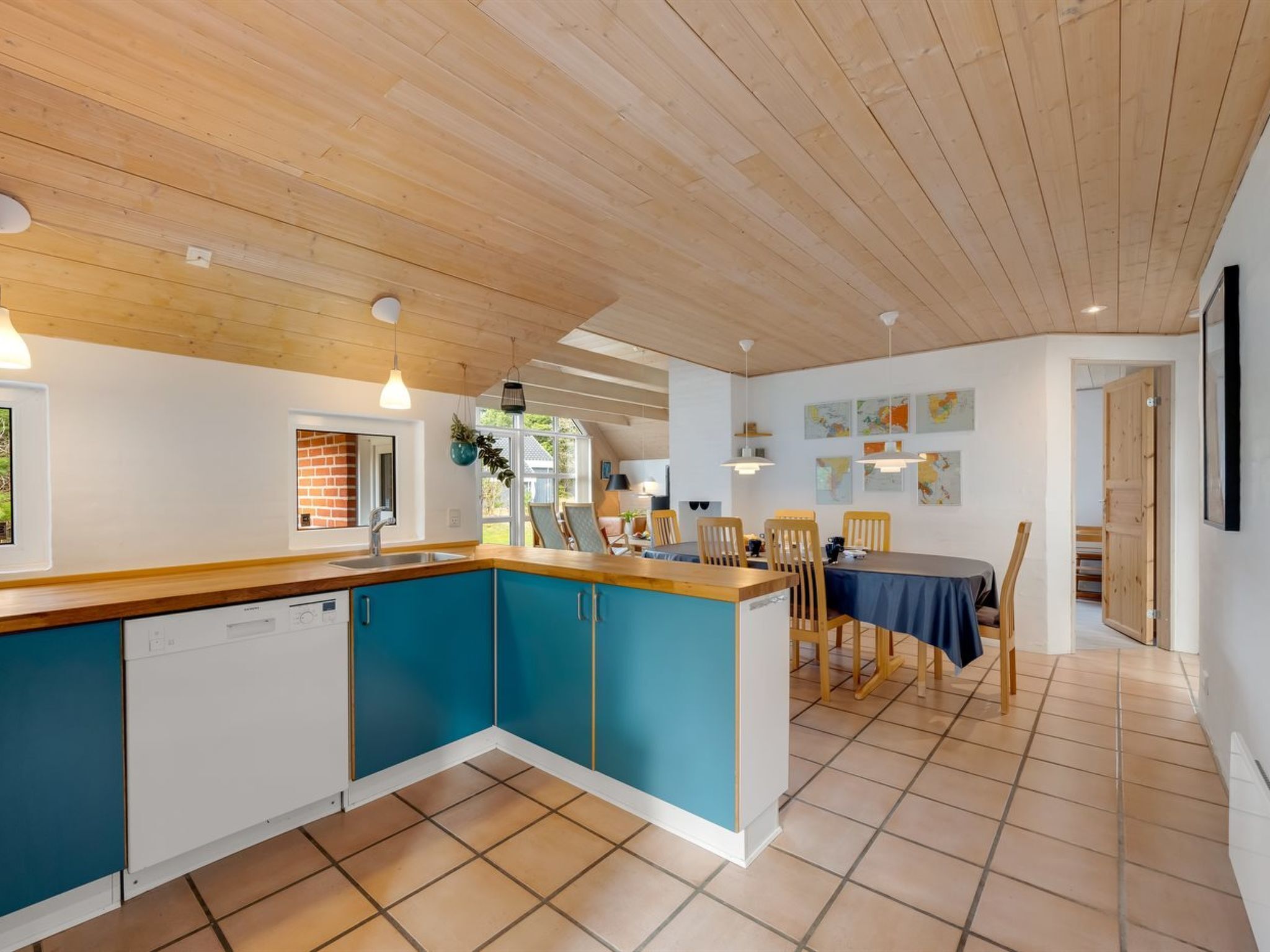 A modern kitchen with a wooden ceiling, blue cabinets, and a dining area with a table and chairs.