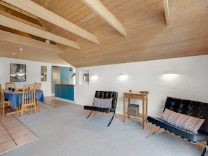 Ein geräumiger Raum mit hoher Decke, einem Essbereich mit blauer Tischdecke, einem schwarzen Ledersofa und einem kleinen Holztisch mit einem Korb.