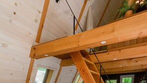 Een knus loft slaapkamer met een houten trap, een comfortabele bank en een groot raam.