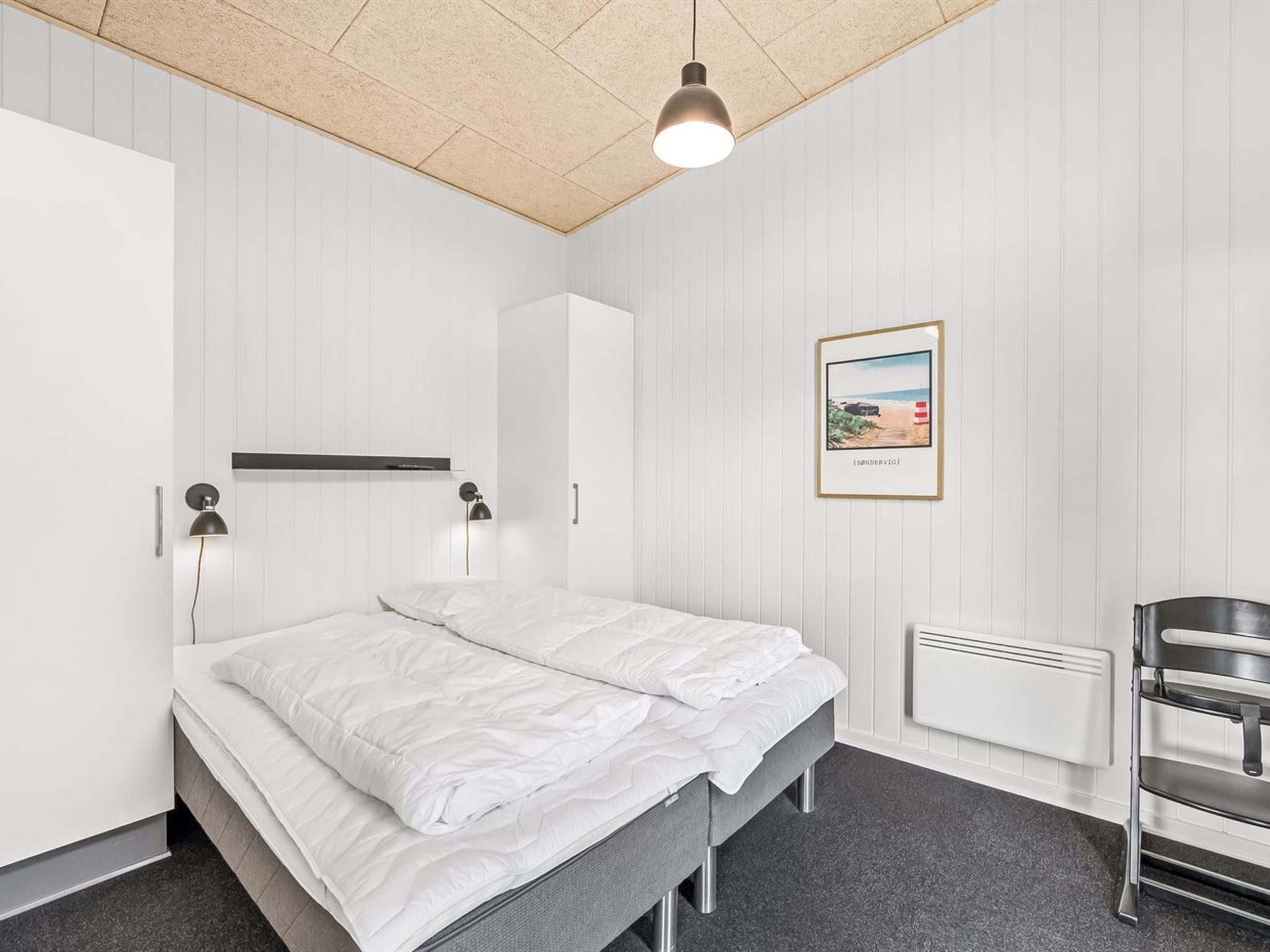 Un dormitorio moderno con cama, lámparas de noche, un cuadro en la pared y un radiador.