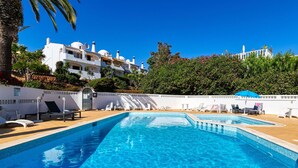 A clear blue pool with lounge chairs and umbrellas, surrounded by white buildings and lush greenery. - Casa Ella - Beautifully renovated luxury townhouse walking distance of Carvoeiro (Carvoeiro)