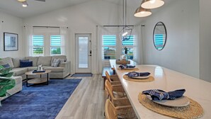 A spacious living area with a sofa, coffee table, and dining table set with placemats and napkins. - New Build! Priv Pool, Firepit, Walk to the Beach | Alright, Alright by AvantStay (Port Aransas)