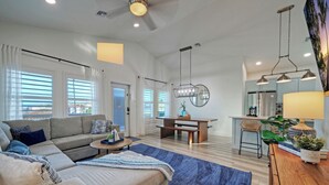 A modern living room with a sofa, coffee table, and a dining area with a bench and table. - New Build! Priv Pool, Firepit, Walk to the Beach | Alright, Alright by AvantStay (Port Aransas)