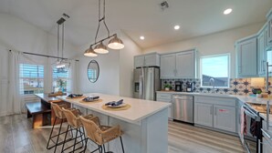A modern kitchen with a central island, bar stools, stainless steel appliances, and light blue cabinets. - New Build! Priv Pool, Firepit, Walk to the Beach | Alright, Alright by AvantStay (Port Aransas)
