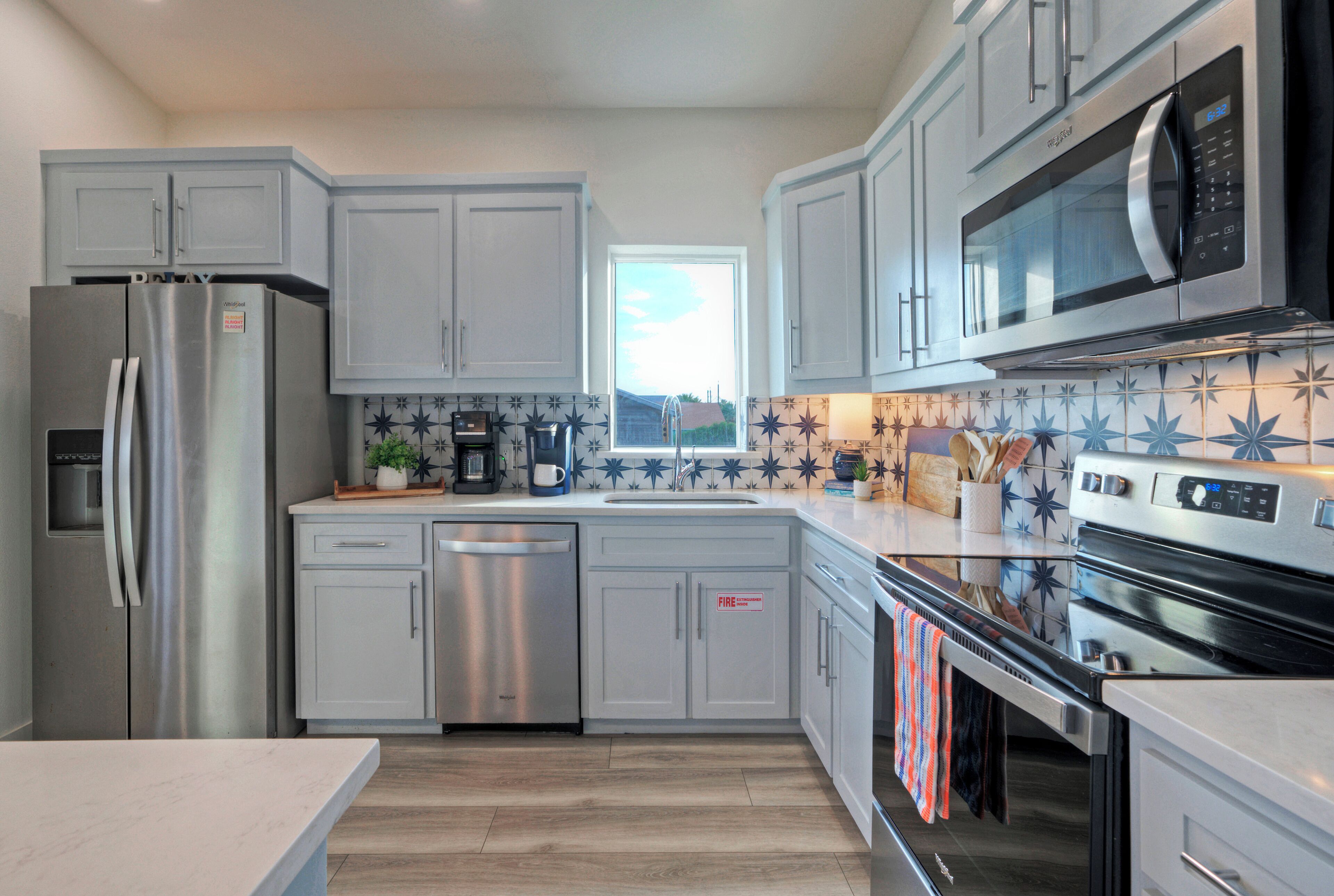 A modern kitchen with stainless steel appliances, grey cabinets, and a tiled backsplash.
