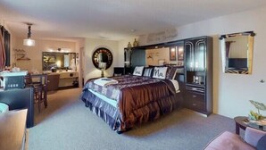 A bedroom with a large bed, a desk, a mirror, and a wardrobe. - Suite Dreams 101 at Tradewinds (Eureka Springs)