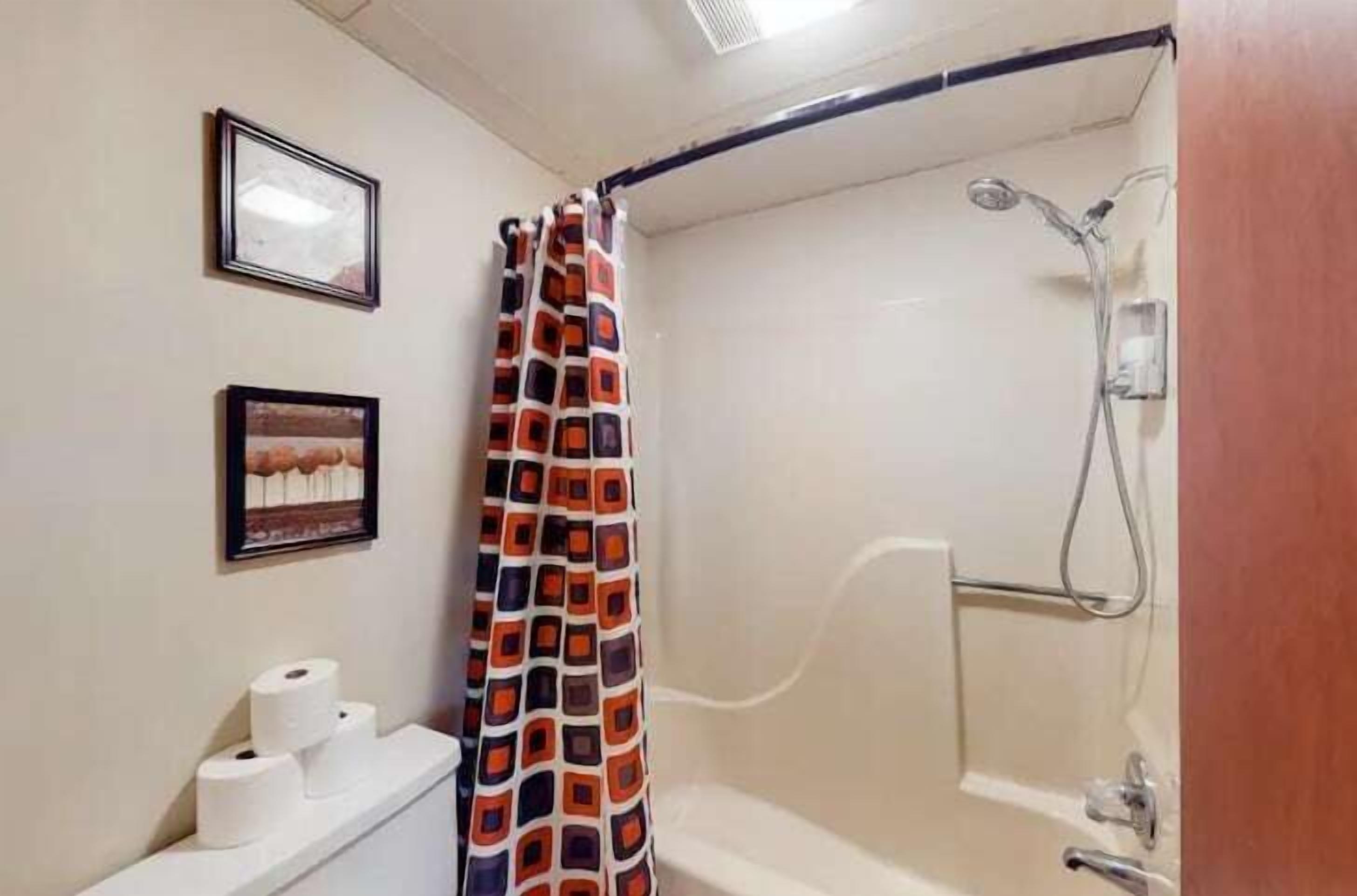Une salle de bain avec une douche, du papier toilette et deux tableaux encadrés accrochés au mur.