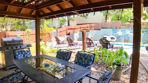 An outdoor patio with a glass-top table and chairs, a barbecue grill, and a pool with lounge chairs and inflatable rings. - Suite Dreams 101 at Tradewinds (Eureka Springs)